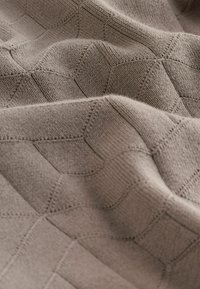 Tissu tricoté marron doux avec un motif géométrique texturé composé de rectangles et d’hexagones interconnectés, présenté en gros plan sur des plis.