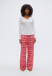 Pantalon de pyjama rouge à motifs avec des flocons de neige blancs, associé à un haut à manches longues gris clair avec un col henley et des boutons.