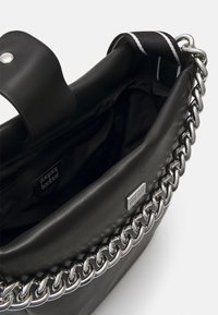 Sac à main en cuir noir avec un accent de chaîne argentée, présentant une poche zippée à l'intérieur, une texture douce et une fermeture à rabat.