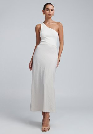 Asymmetrisk hvid ribbet top parret med en glat, lysegrå maxiskørt. Skørtet har et subtilt struktureret mønster. Lysebrune sandaler.