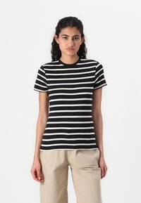 T-shirt a righe bianche e nere con colletto tondo e maniche corte, realizzata in tessuto morbido, abbinata a pantaloni beige chiaro.
