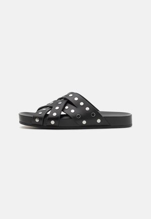 Zwarte slidesandalen met kruislings gespen versierd met zilverkleurige studs, een platte zool en een soepele leren textuur.