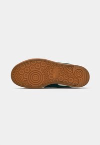 Rubber sneaker sole with a textured brown surface, circular patterns, and a logo. Dark green upper with white accents along the side.