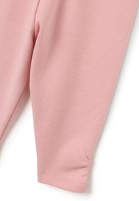 Nahaufnahme eines sanft rosa Stoffbeins mit glatter Stricktextur und gerafftem Nähdetail nahe dem Saum.
