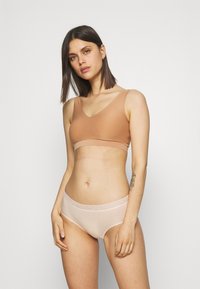 Soutien-gorge beige sans couture avec des bretelles larges et un décolleté en V ; associé à une culotte rose clair avec une bordure en dentelle à la taille. Texture lisse.