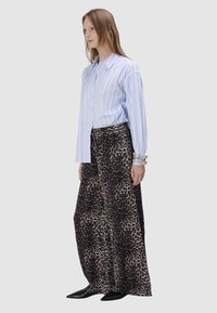 Gestreepte blauwe button-up overhemd met lange mouwen, gecombineerd met vloeiende brede leren broek met luipaardprint, en zwarte puntige schoenen. Zilveren armbanden gedragen.