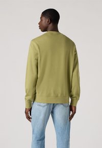 Sudadera verde con cuello redondo y puños acanalados, combinada con jeans de mezclilla azul claro, que destacan un ajuste relajado y una textura suave.