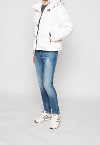 Hvid dunjakke med hætte og et lille logo. Kombineret med lyseblå slidte jeans og hvide sneakers med lyserøde detaljer.