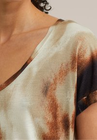 Sukienka satynowa z dekoltem w serek, w kolorze kremowym z brązowymi abstrakcyjnymi wzorami. Krótkie rękawy i gładka tekstura.