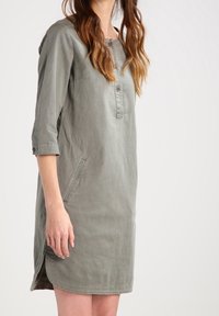 Harmaa, löysä mekko, jossa on kolmannes hihasta, nappiyksityiskohta kaula-aukossa ja sivutaskut. Valmistettu pehmeästä, teksturoidusta kankaasta.