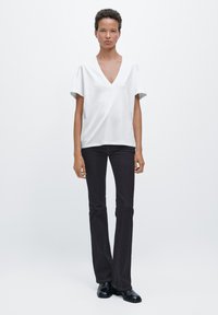 Witte katoenen T-shirt met V-hals en korte mouwen, gecombineerd met donkerblauwe denim flared broek en zwarte schoenen. Eenvoudig ontwerp en een ontspannen pasvorm.