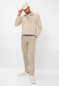 Beiger Zip-Hals-Pullover, beige Hose und helle Sneaker. Das Outfit zeichnet sich durch einen entspannten Schnitt und eine einfarbige Farbgebung für einen minimalistischen Look aus.