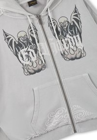 Light gray zip-up hoodie with winged skeleton graphics and white stylized text on chest, front pocket, and drawstring hood.