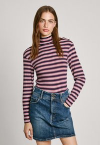 Suéter de cuello alto a rayas en rojo, blanco y azul combinado con una falda mini de mezclilla de tiro alto. Tela suave con textura acanalada y cierre de botones.