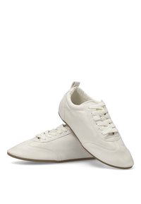 Zapatillas de cuero blanco con una superficie texturizada, puntera redondeada y suela plana de goma. Presenta un sistema de cordones tradicional y una lengüeta en el talón.
