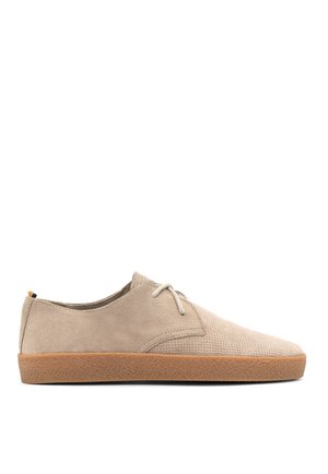 Zapatos de ante beige con un diseño perforado, punta redonda y suela de goma marrón claro. Presentan cierre con cordones y un detalle sutil de marca.