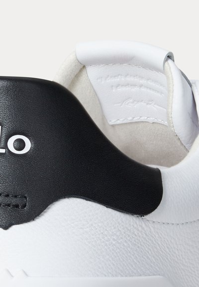 Valge nahast tossu konts lähedalt, millel must nahast plaastriga osa valgest logost ja pehmendatud krae, millel on reljeefne kiri.