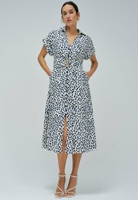 Bílé šaty s límcem a námořnickými abstraktními skvrnami, krátké rukávy, páskový pas a přední rozparek. Hladká tkanina s uvolněným střihem.