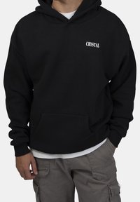 Sudadera negra con bolsillos tipo canguro, puños acanalados y un logo blanco de "CRYSTAL" en el pecho. Hecha de material de algodón suave.