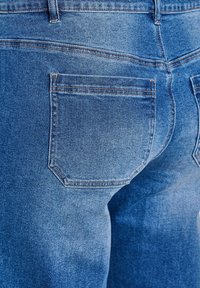 Modré riflové nohavice s vyblednutým efektom, s nášivkovým vreckom a výrazným prešitím pozdĺž pásu a vreciek.