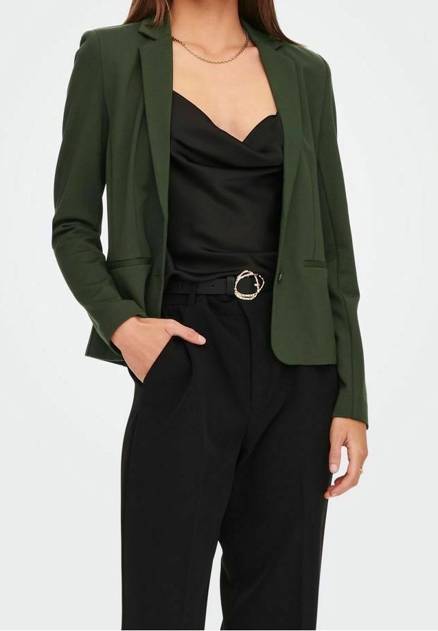 Femme portant un blazer vert foncé sur un caraco en satin noir, pantalon noir taille haute avec une ceinture noire avec boucle dorée.