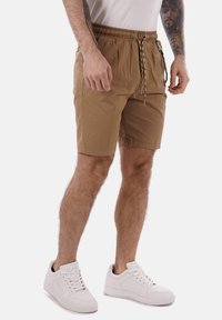 Pantaloni corti color sabbia realizzati in tessuto leggero, con vita elasticizzata e cordoncino, tasche laterali e vestibilità casual. Abbinati a sneakers bianche.