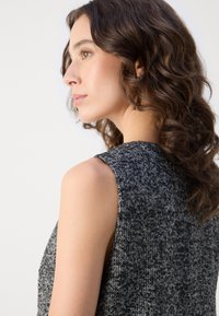 Mouwloze grijze tweed jurk met een gestructureerd oppervlak, voorzien van een hoge halslijn en een getailleerd silhouet. Subtiele details op de schouder.