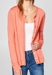 Korálový kardigan vyrobený z lehkého materiálu, s kulatým výstřihem, knoflíkovým zapínáním, žebrovanými manžetami a přiléhavým střihem.