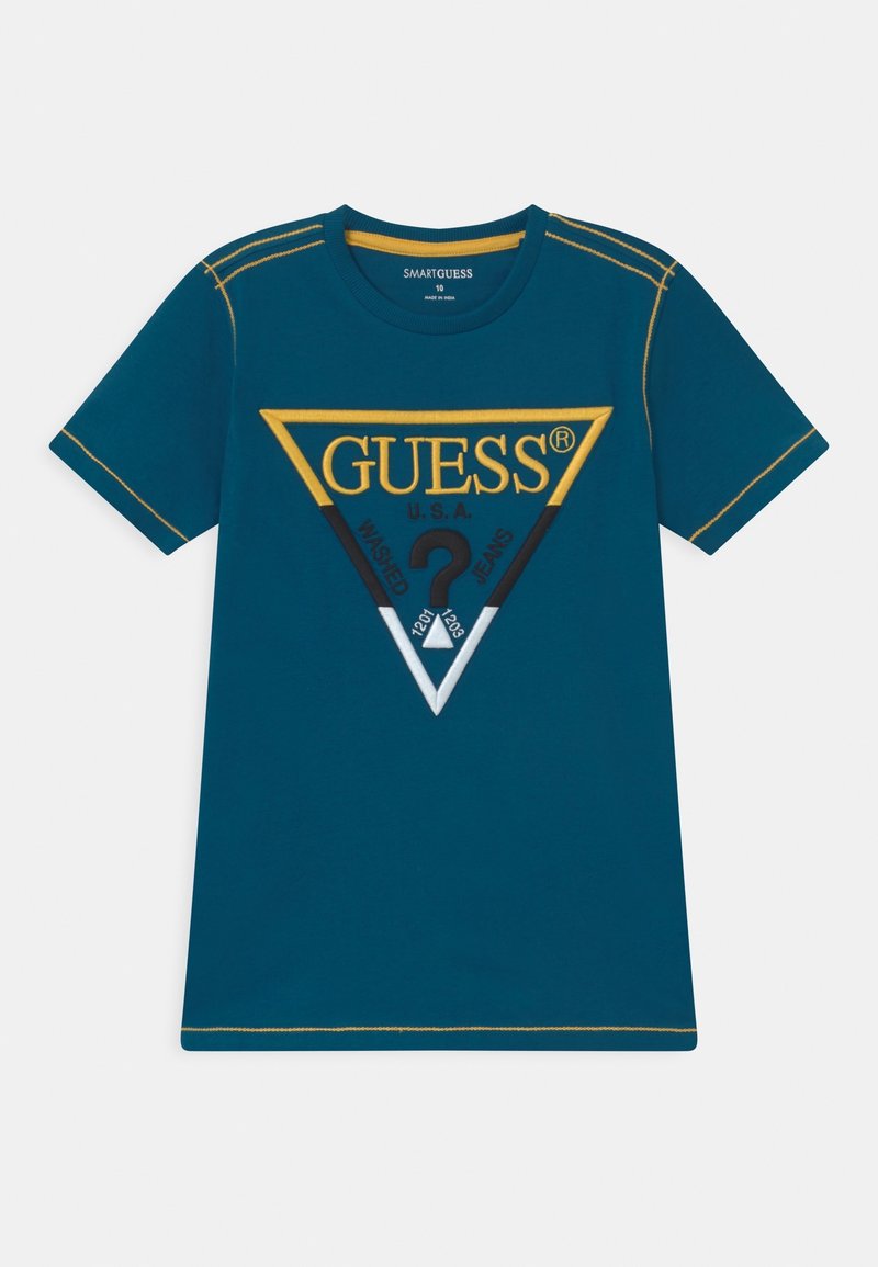 T-shirt à manches courtes bleu sarcelle avec des coutures jaunes et un grand logo triangulaire portant la mention "GUESS U.S.A." avec des motifs et du texte à l’intérieur du triangle.
