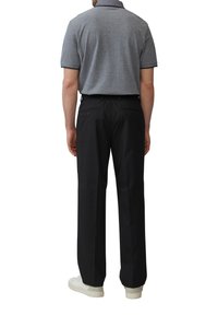 Grijze polo met korte mouwen, zwarte broek en witte sneakers. De broek heeft een relaxte pasvorm en achterzakken.