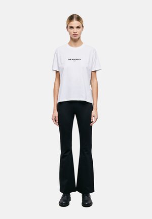 T-shirt bianca in cotone a maniche corte, con il logo nero "THE KOOPLES" centrato sul petto. Abbinata a pantaloni neri a palazzo.