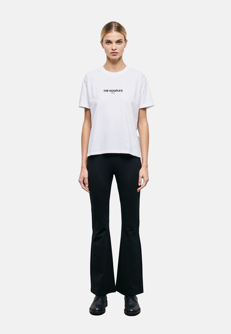Baltas kokvilnas T-krekls ar īsām piedurknēm, ar melno logo tekstu "THE KOOPLES", kas centrēts uz krūšu daļas. Saskaņots ar melnām platu kāju biksēm.