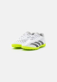 Scarpe da calcio bianche con superficie testurizzata, strisce nere e suole gialle fluorescenti. Presentano perforazioni per la traspirazione e un design aerodinamico.