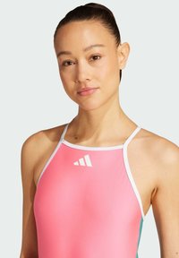 Vaateurheilupuku vaaleanpunaisena, jossa on kaulakosketusdesign, valkoisia yksityiskohtia ja logo rinnassa. Sileä tekstuuri ja istuva muoto.