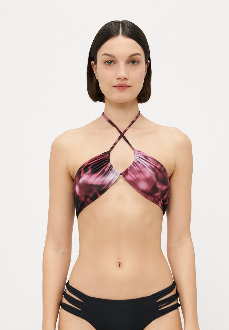 Halter-Bikini-Oberteil mit pinkem und schwarzem abstraktem Muster, verfügt über gekreuzte Träger und geraffte Details, getragen mit schwarzem Bikini-Unterteil mit Ausschnitten.