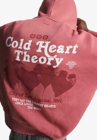 Maroon pullover hoodie featuring large text "Cold Heart Theory" and a graphic of hearts on the back. Soft fabric, relaxed fit, and kangaroo pocket.