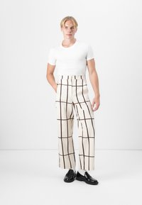 Pantaloni a gamba larga crema con motivo a quadri marrone, vita alta e tasche laterali; abbinati a una t-shirt bianca aderente e mocassini neri.