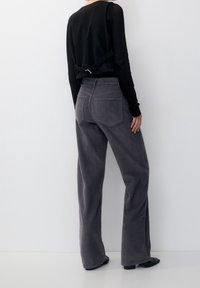 Pantalons en velours côtelé gris à jambes larges avec poches arrière, associés à un haut noir à couches avec un détail de boucle à la taille.