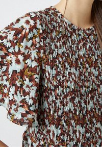 Blommig smockad klänning med en blandning av blå, brun och senapsfärgad. Texturerad tyg med rynkad detalj runt halsringningen och ärmarna.