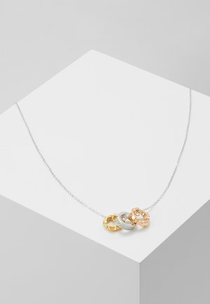 Collier en chaîne argentée avec trois anneaux entrelacés en or, argent avec diamants, et or rose sur une surface géométrique blanche.