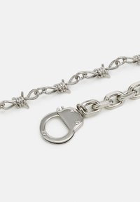 Silver chain bracelet with barbed wire design elements. Features a large clasp and smooth metallic finish. Distinctive links and accents.