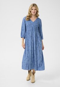 Abito midi blu con motivi floreali, scollatura a V e corpetto arricciato. Maniche lunghe e design della gonna fluida. Indossato con stivali alla caviglia color beige.