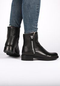 Botines de cuero negro con un acabado texturizado, que presentan un cierre lateral y un tacón bajo. Combinados con jeans azules.