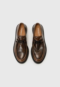 Chaussures en cuir marron avec une finition lisse, bout rond et semelle en caoutchouc noir. Présente des lacets et un nom de marque embossé sur la semelle intérieure.