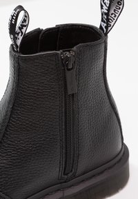 Bottine noire en cuir texturé avec fermeture éclair latérale, languettes de tirage marquées au niveau du talon et du col, et semelle en caoutchouc épaisse avec coutures visibles.