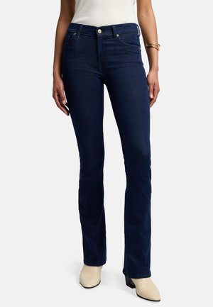 Dunkelblaue ausgestellte Jeans aus Denim mit hoher Taille, vorderen Taschen und Knopfverschluss. Kombiniert mit hellen Stiefeletten.