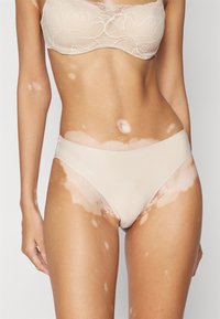 Beige seamless underwear with a smooth texture, low-rise cut, and subtle side detailing, set against a light background.