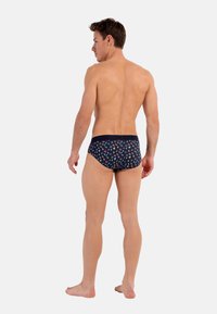 Marinefarbene Schwimmslip mit einem bunten Blumenmuster, elastischem Bund, körpernahem Schnitt und glatter Textur, von hinten gezeigt.