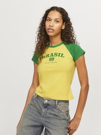 Žluté a zelené tričko s krátkým rukávem se textem "BRASIL" a grafikou vlajky. Tričko má úzký střih a kulatý výstřih.