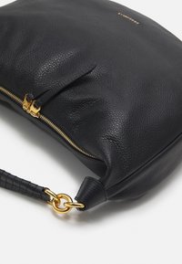 Sort læderhandtaske med en tekstureret overflade, gylden lynlås og et flettet håndtag. Har en metallisk ringdetalje.